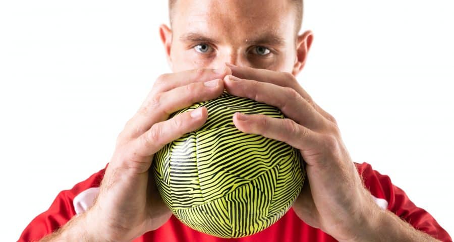 Confident young male caucasian handball player holding green ball against white background