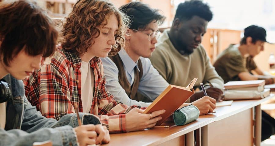 Row of multicultural teenage students of university sitting by desk at lecture