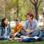 Teacher with small children sitting outdoors in city park, learning group education concept