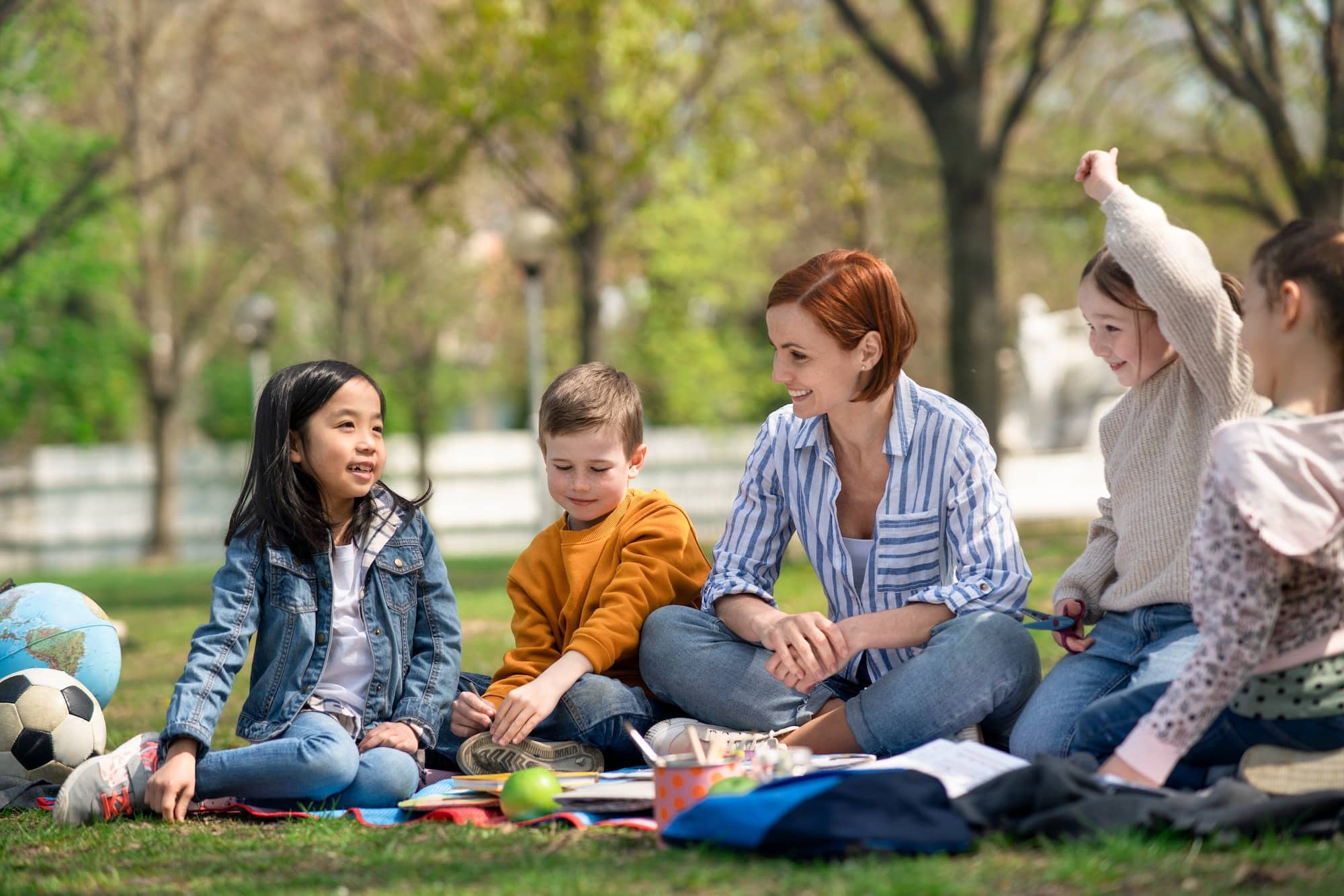Teacher with small children sitting outdoors in city park, learning group education concept